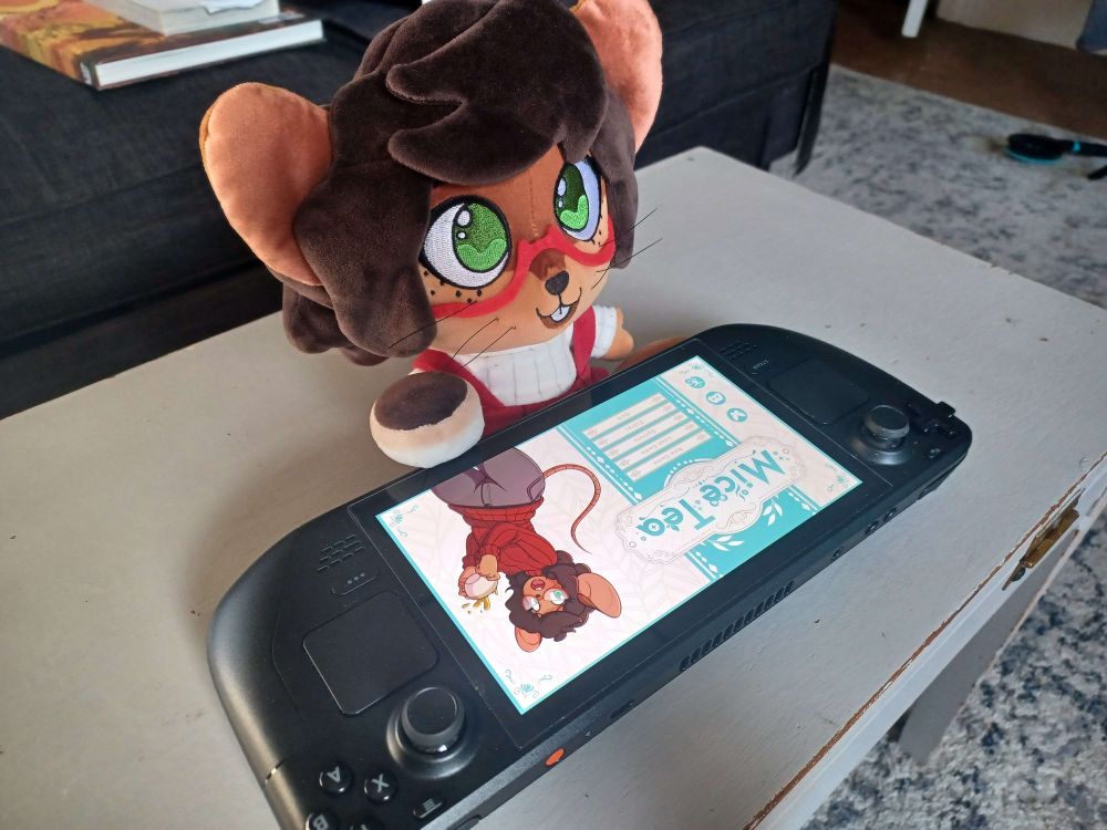 A plush of Margart de Campos, a brown-furred mousegirl with glasse, plays Mice Tea on a Steamdeck. The title screen shows her holding a cup of tea, just like the plush.