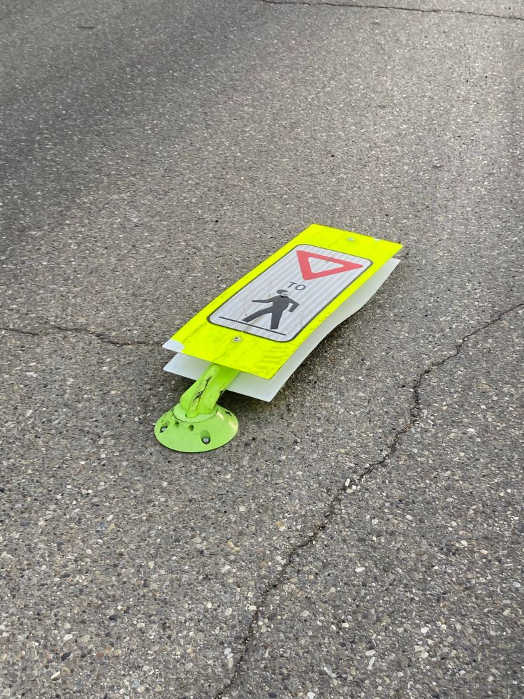 A neon yellow “Yield to pedestrians” sign flattened on the road