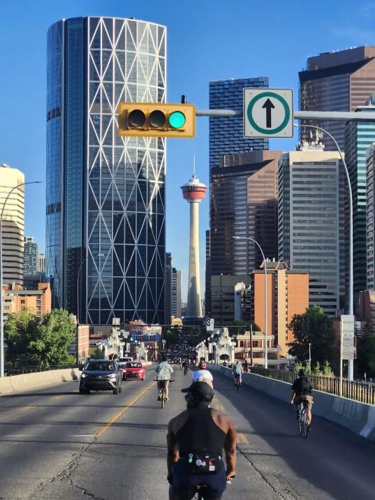Several folks on bicycles bike down centre street. The Bow and Calgary Tower in the background. 