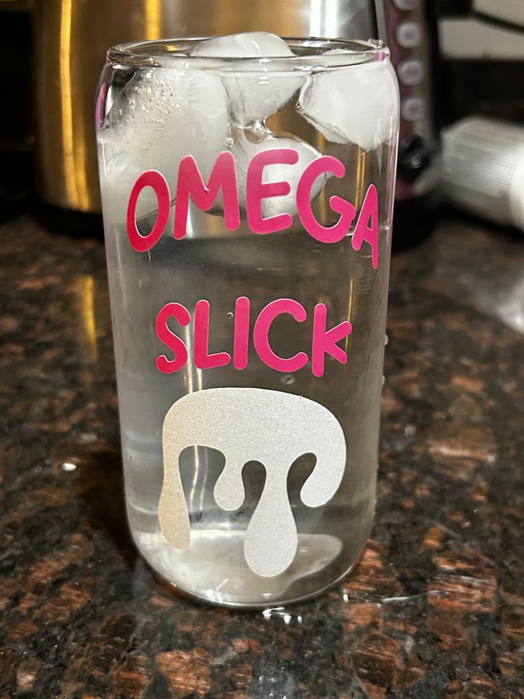 a glass can cup that says "omega slick" in color changing vinyl (white in warm temp and pink in cold temps) with a dripping glob in sparkly white vinyl.