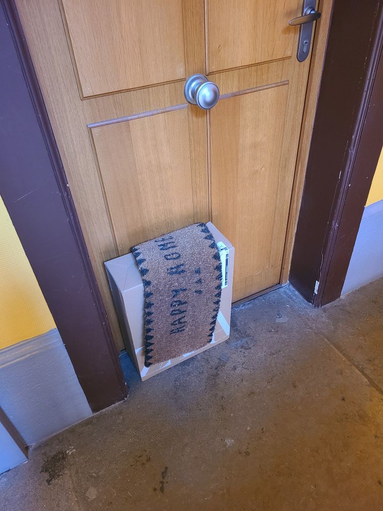 Un gros colis recouvert du paillasson devant une porte. 