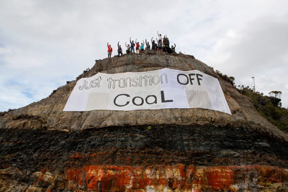 Activists stand at the top of a coal face above a banner saying Just Transition Cool Off