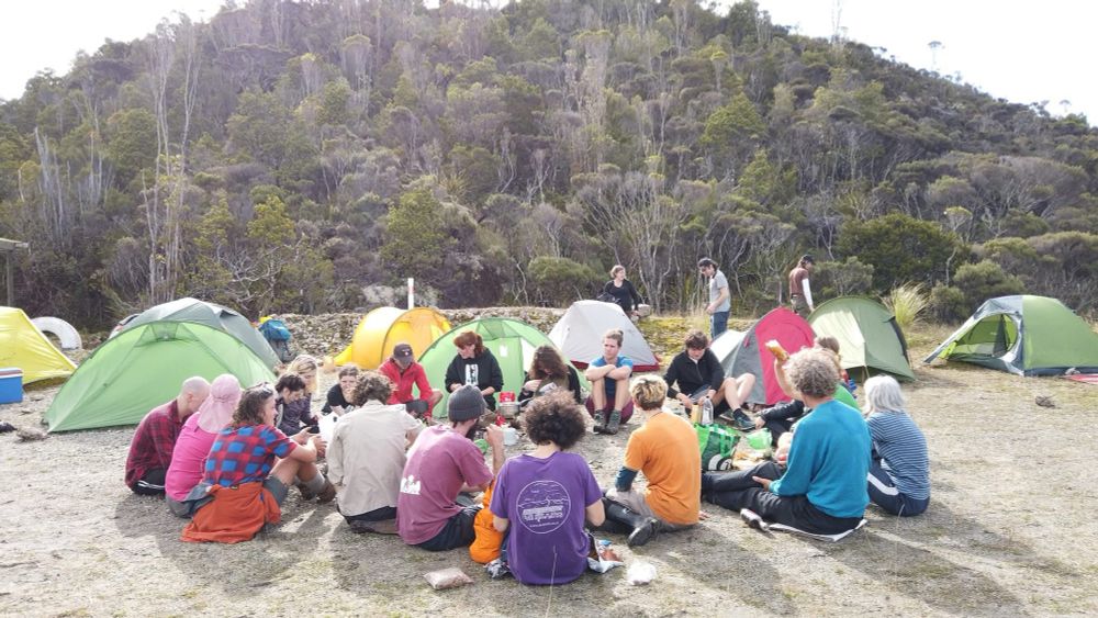 Activists at their camp sit in a circle, against a bushclad background 