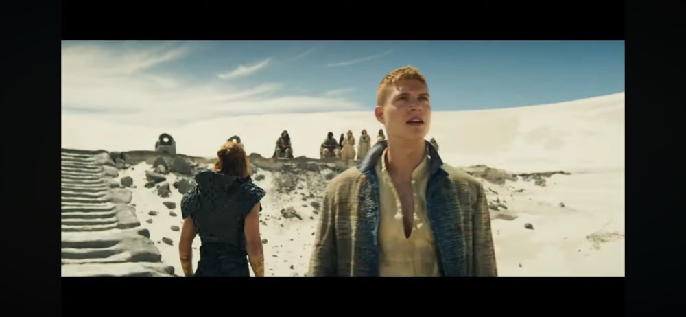 Rand and another man stand in what we see in another overhead shot to be Al’Cair Dal. The other man beside Rand has twin dragon tattoos and is standing in the center with him, with sleeves removed so his arms are showing. He has red hair that goes to his shoulders and looks pulled half-up with a bun.