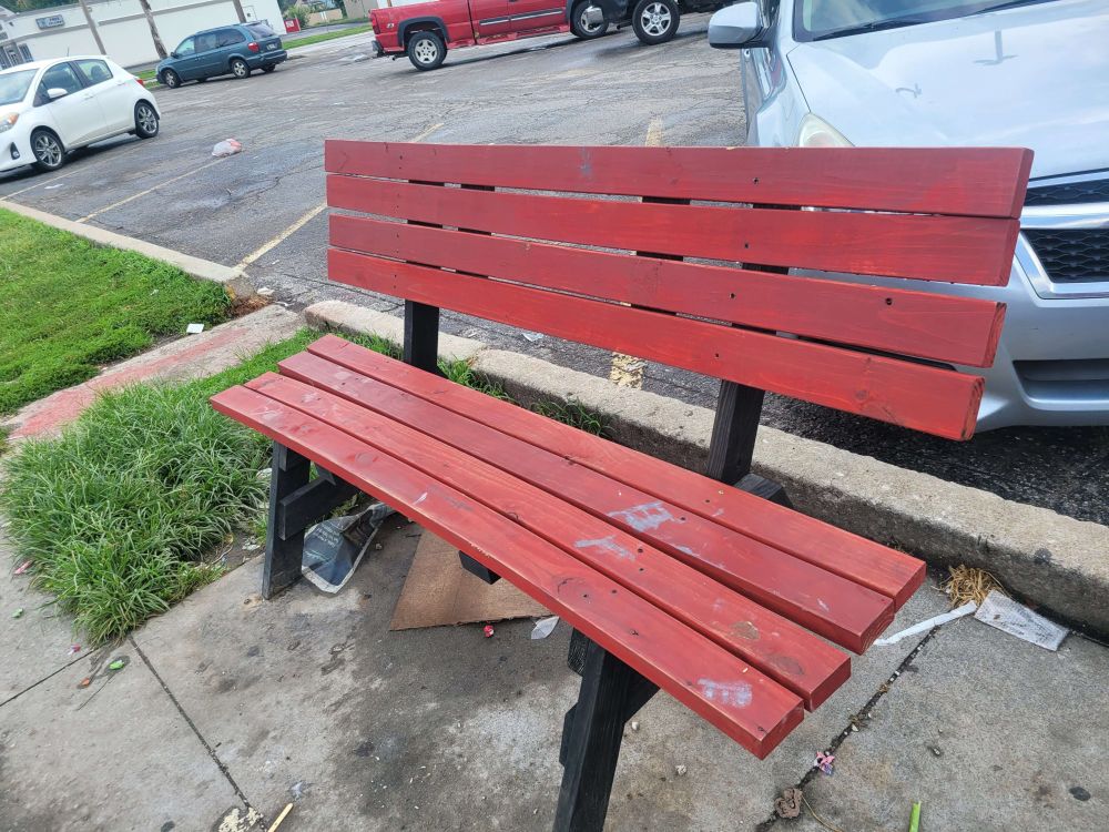 A wooden red and black bench at a bus stop.