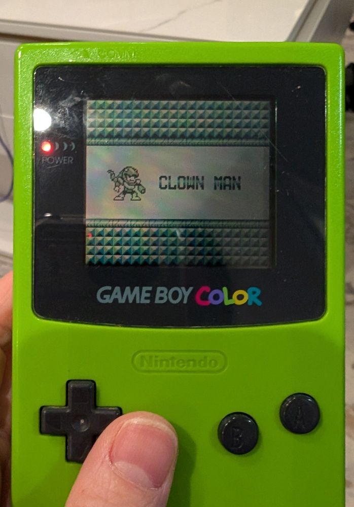 A photo of a lime green Game Boy Color with a bootleg MegaMan game. The screen shows a picture of SnakeMan with the words "CLOWN MAN" next to him.