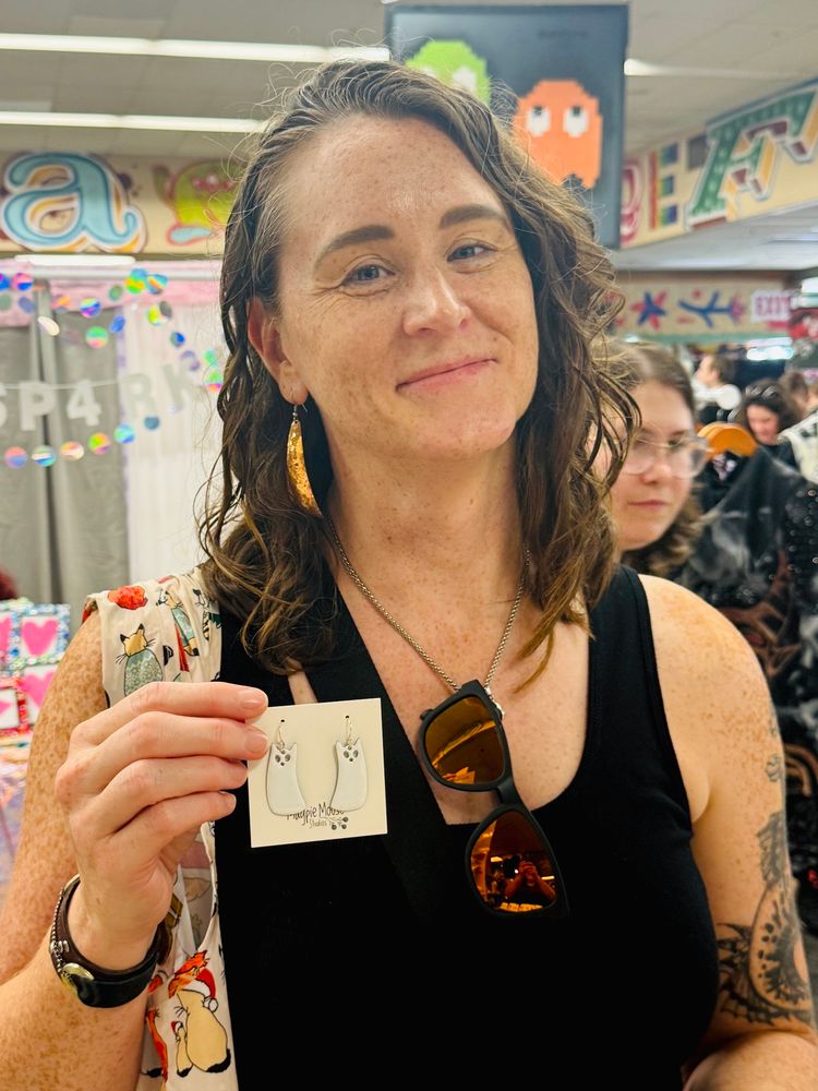 A person holding a pair of enamel earrings by Magpie Mouse Studios