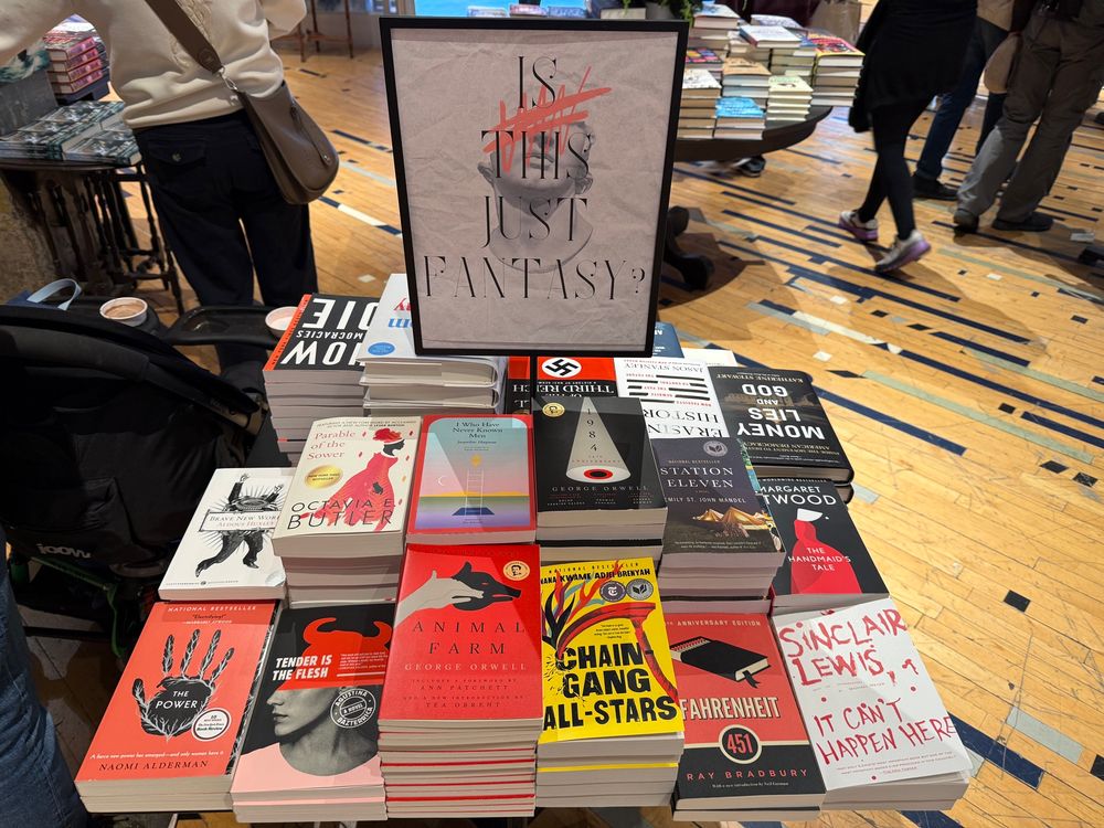 Sign: IS THIS JUST FANTASY? 

Books include; It Can’t Happen Here, 1984, Fahrenheit 451, The Handmaid’s Tale