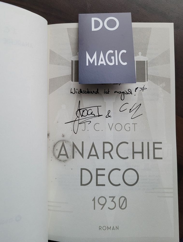 Widmung und Unterschriften der Vögte im Buch Anarchie Deco 1930: "Widerstand ist magisch" mit einem "Do Magic"-Lesezeichen.
