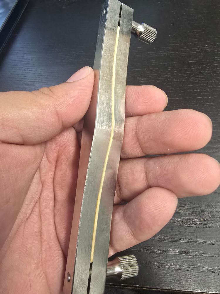 A hand holds a metal bassoon shaper. A piece of arundo donax cane can be seen flush with the contours of the shaper, indicating the cane's shape conforms to the shaper's