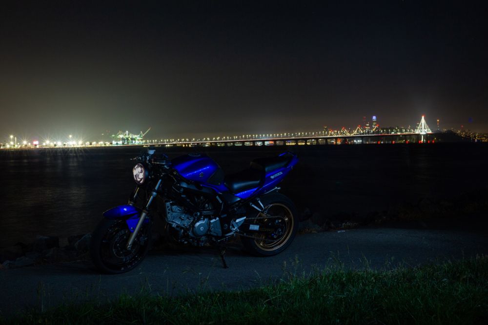 Blue motorcycle with port of Oakland and bay bridge behind it 