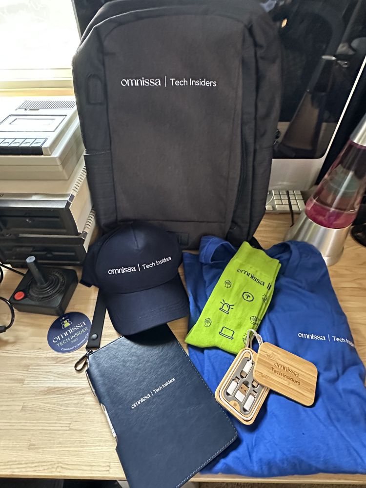 omnissa goodies - a backpack, hat, sticker, notebook, socks, a tshirt and handy usbc port converter pack... also in background, functioning atari disk drives, a joystick, old imac and lava lamp that were not in the box