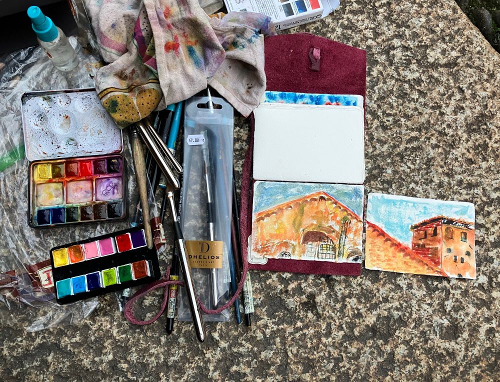 Pleinère studio on location at Milan’s Sant’ Abrogio, pictures in my painting. Two palettes of watercolor, paintbrushes, old tea towels for wiping brushes, a small Spray bottle and a leather notebook of watercolor paper that travels with me. This was all on the cement floor as I painted from late afternoon into evening.