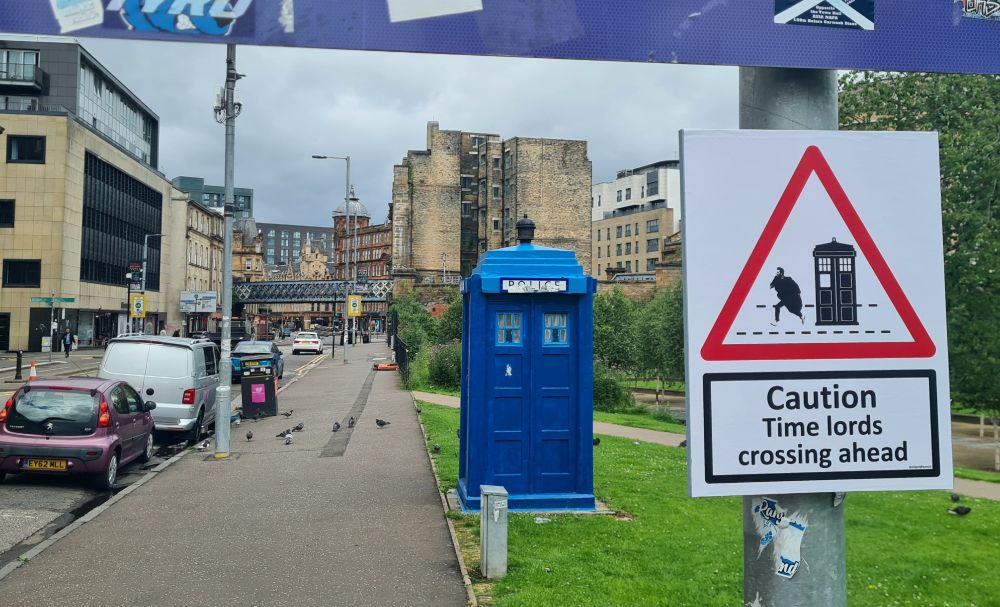 Blue police box TARDIS, with sign 'Caution Time lords crossing ahead'