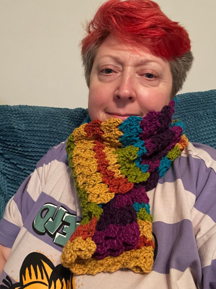 Selfie of Madder wearing a crochet scarf in stripes of yellow, orange, green, blue and purple. 