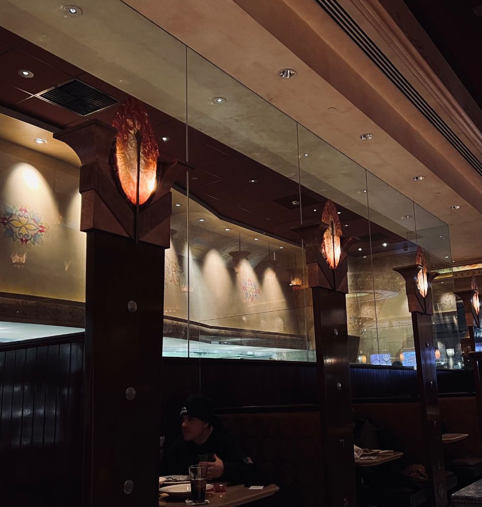 Restaurant booths each have a pillar between them that has an orange oblong leaf shaped light on top that looks like the eye of Sauron, but in a cheesecake factory