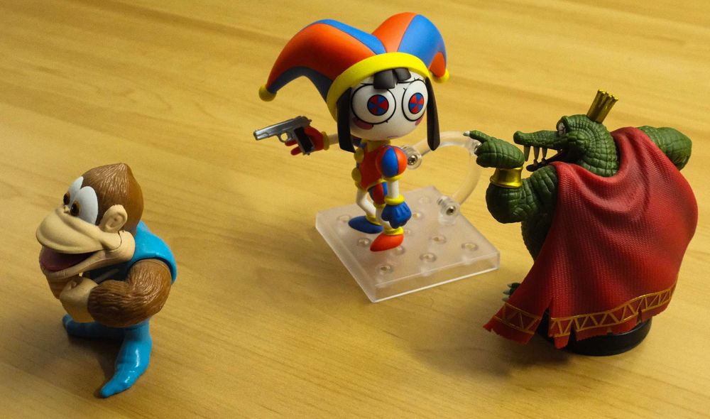 Pomni has a gun. K. Rool asks her to shoot a baby. She really should stop hanging out with these terrible, toothy, chums.

( Pomni is a Nendoroid, K. Rool is an Amiibo, Kiddy Kong is a Toysite, The Gun is from a Joker Persona figure )