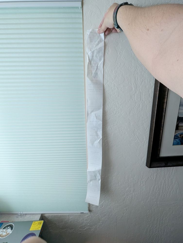 A very long receipt from CVS held against a wall, turned backwards so the items purchased cannot be seen