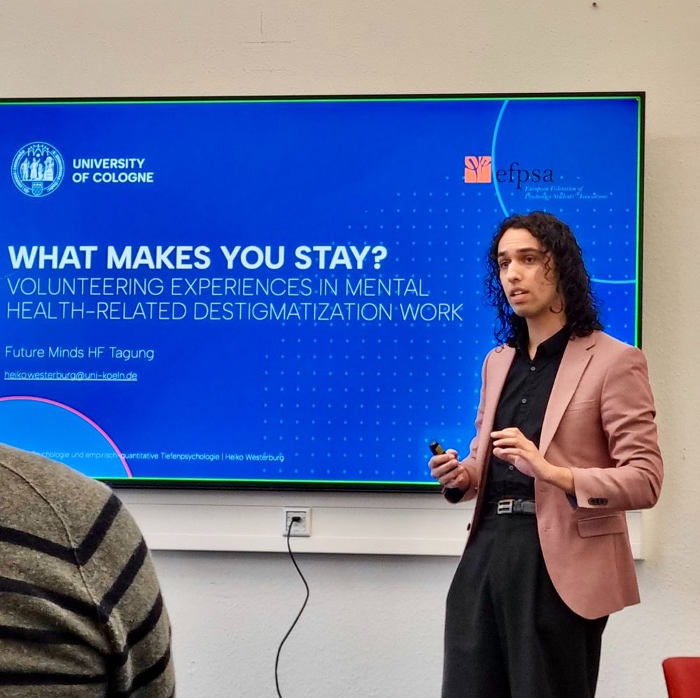 conference room, tv screen showing white text on blue background: "what makes you stay? volunteering experiences in mental health-related destigmatization work". university of cologne and european federation of psychology students association's logos on the slide. in front, the speaker.