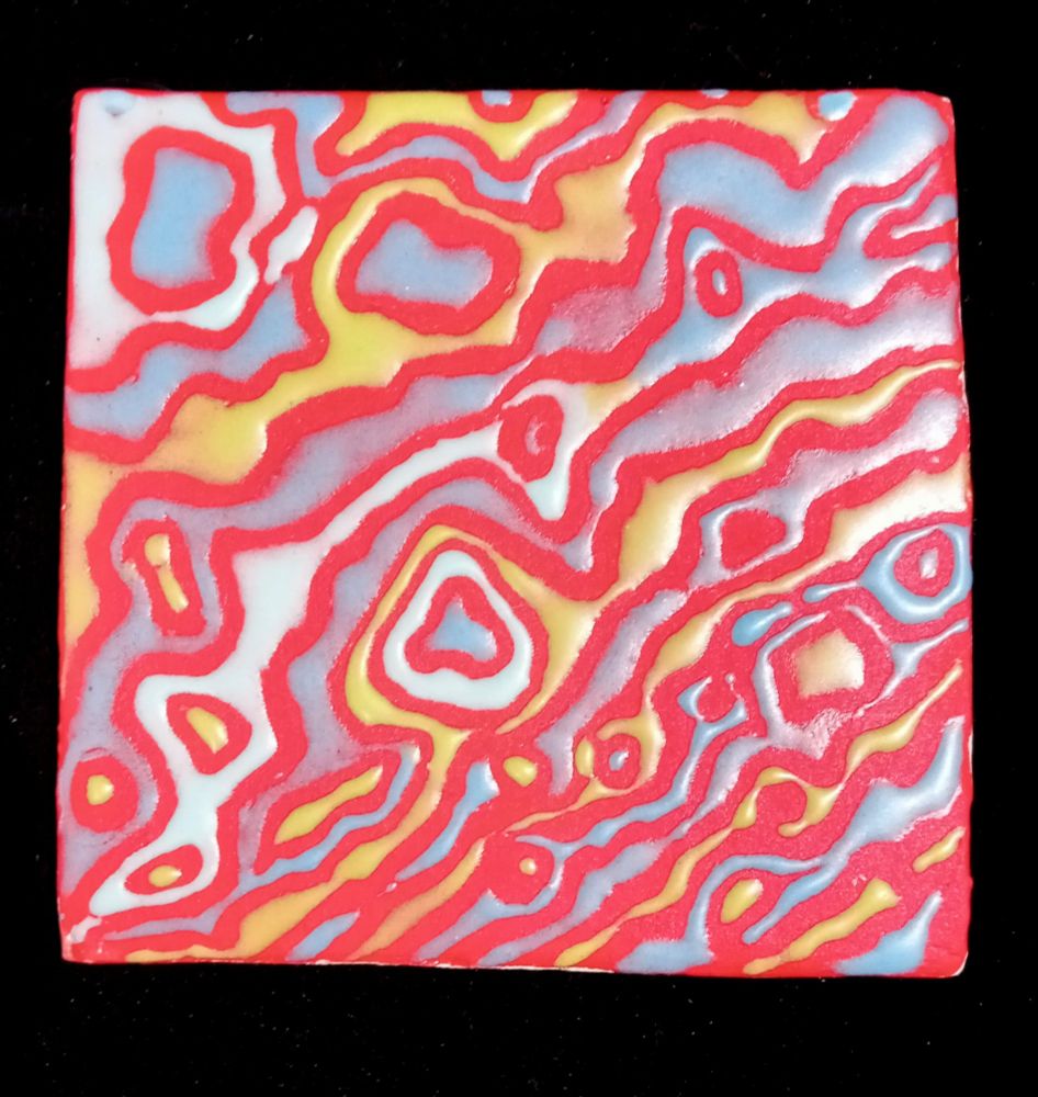 Tile decorated in random patterns of blue and green on a red background. 