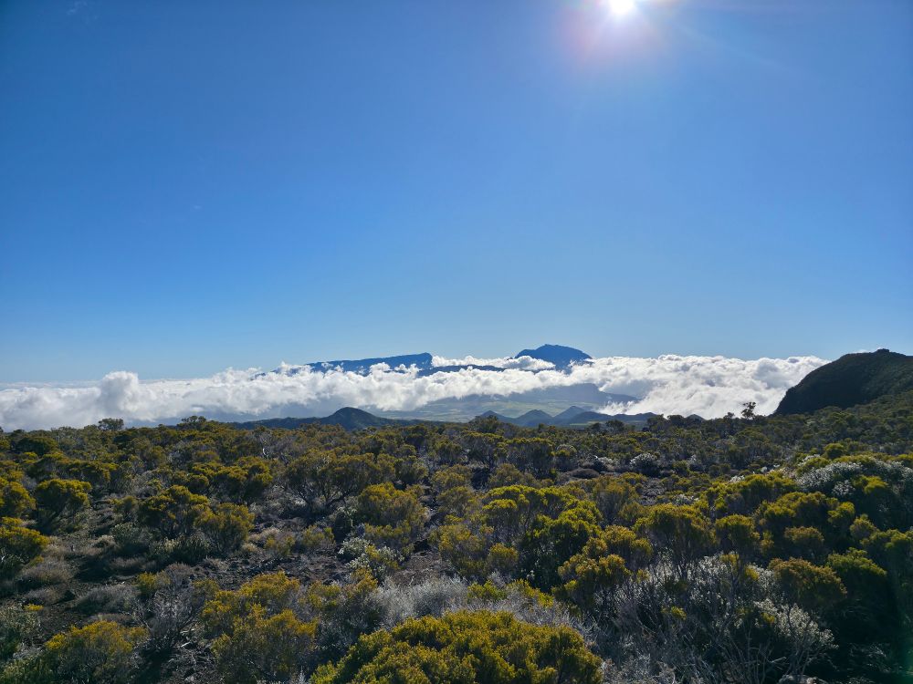 viewpoint of Cilaos and pitons des Neiges, bathed in clouds, under a sunny bright sky.