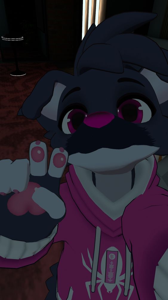 A black and white dog with a hot pink nose, eyes and bubblegum paws faces the camera with a peace sign. They wear a hot pink hoodie with a spider symbol on it that bears a spotify qr code on it