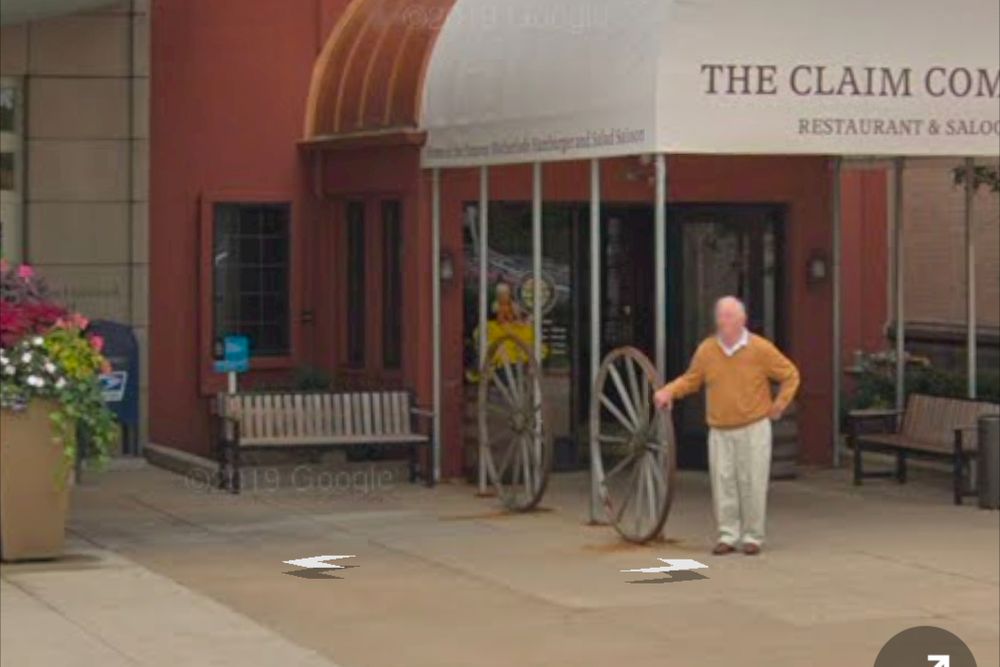 Man wearing a sweater standing outside the old Claim Company restaurant outside the Northbrook Court mall while grasping one of their decorative wagon wheels