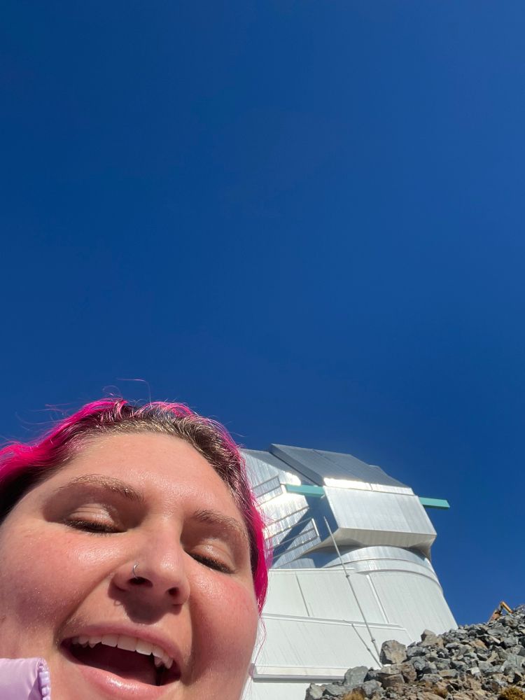 me smiling outside with the rubin dome! two bars that support the dome opening are the same teal as SOAR