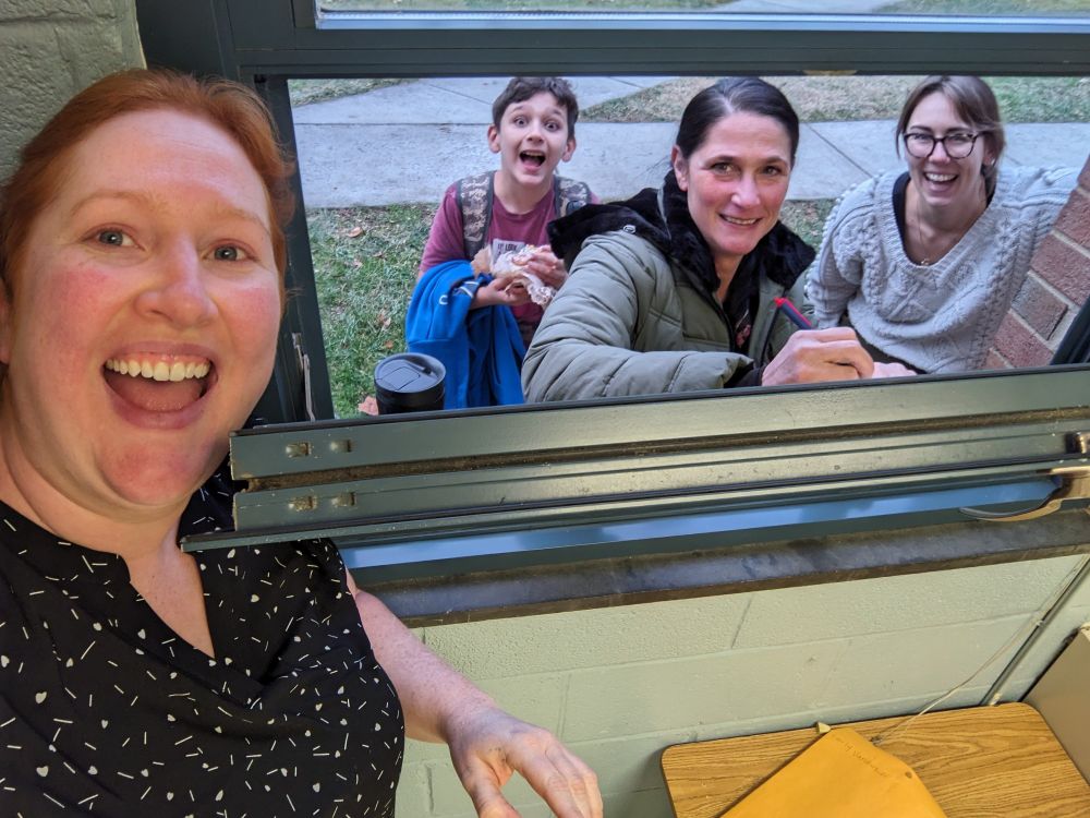 Me standing at my open classroom window with my colleague, her son, and our union organizer standing outside the window. We are all smiling excitedly. Amy has a pen in her hand and is pressing on the window to sign her union authorization card.