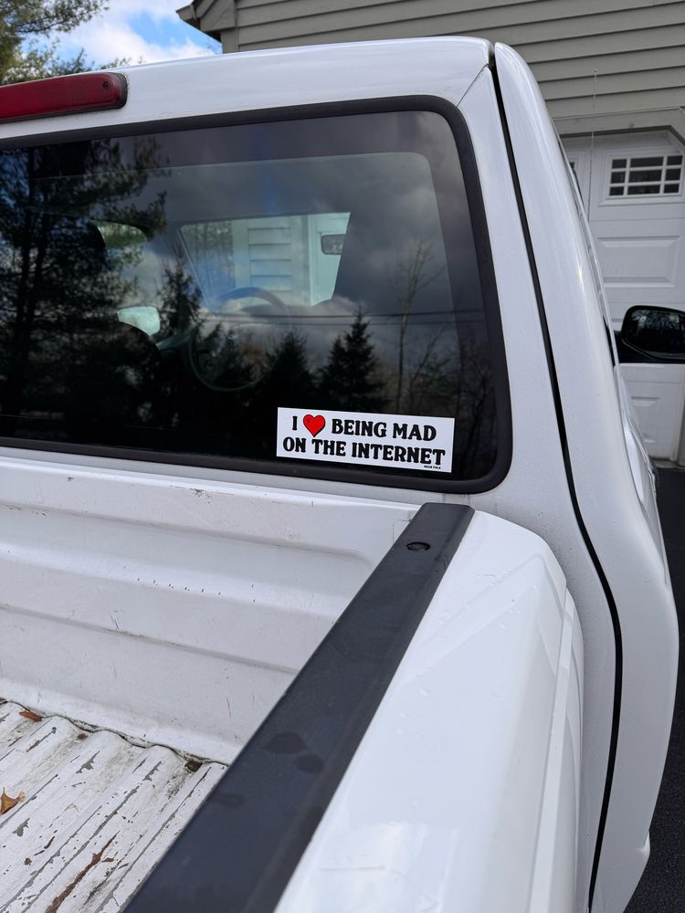 An older white truck with a sticker that says “I love being mad on the internet” on the rear windshield
