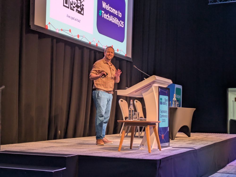 Neil Harrod-Beck smiles on the TechAbility stage as he delivers his chair's speech