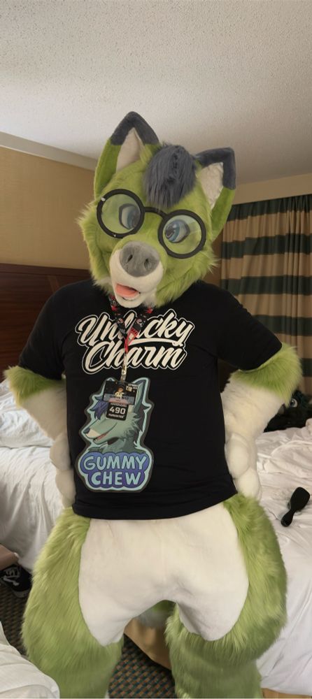 Gummy posing for a picture in his dead dog dance outfit from FurPoc 2024. He is wearing his glasses and a black t-shirt that says “unlucky charm”