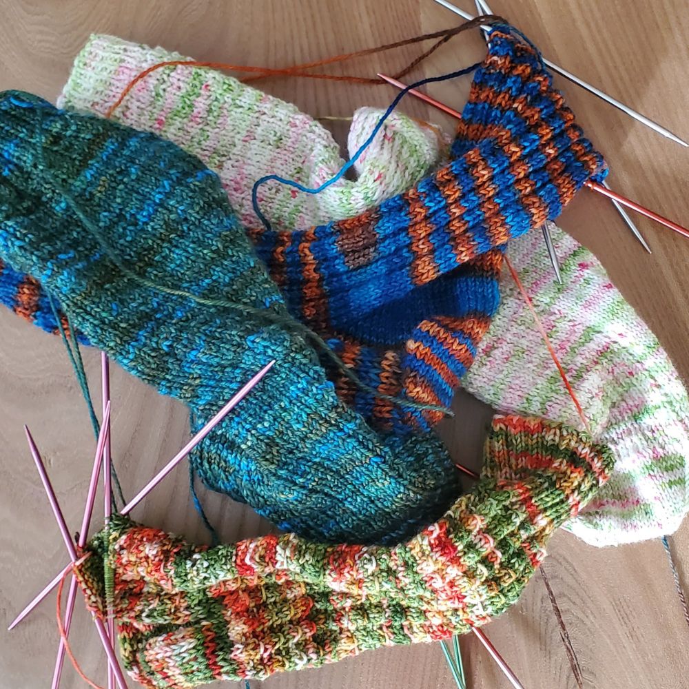 A pile of colorful socks still on the needles sits on a wooden table.