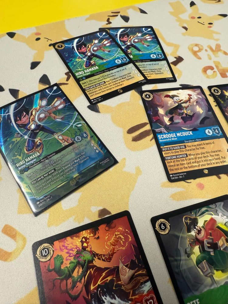 Pikachu mat with lorcana cards on it, including the promo Hiro Hamada enchanted card for getting into the Top 8.