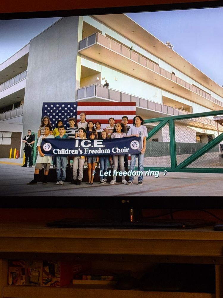 Screenshot of shameless season 9: ep 9 detained migrant children sing “my country tis of thee” in front of American flag as “ice children’s freedom choir”
