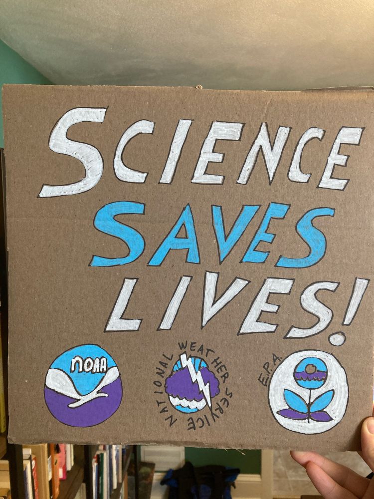Cardboard sign stating “Science Saves Lives” with the logos of the National Oceanic and Atmospheric Administration, the National Weather Service, and the Environmental Protection Agency 
