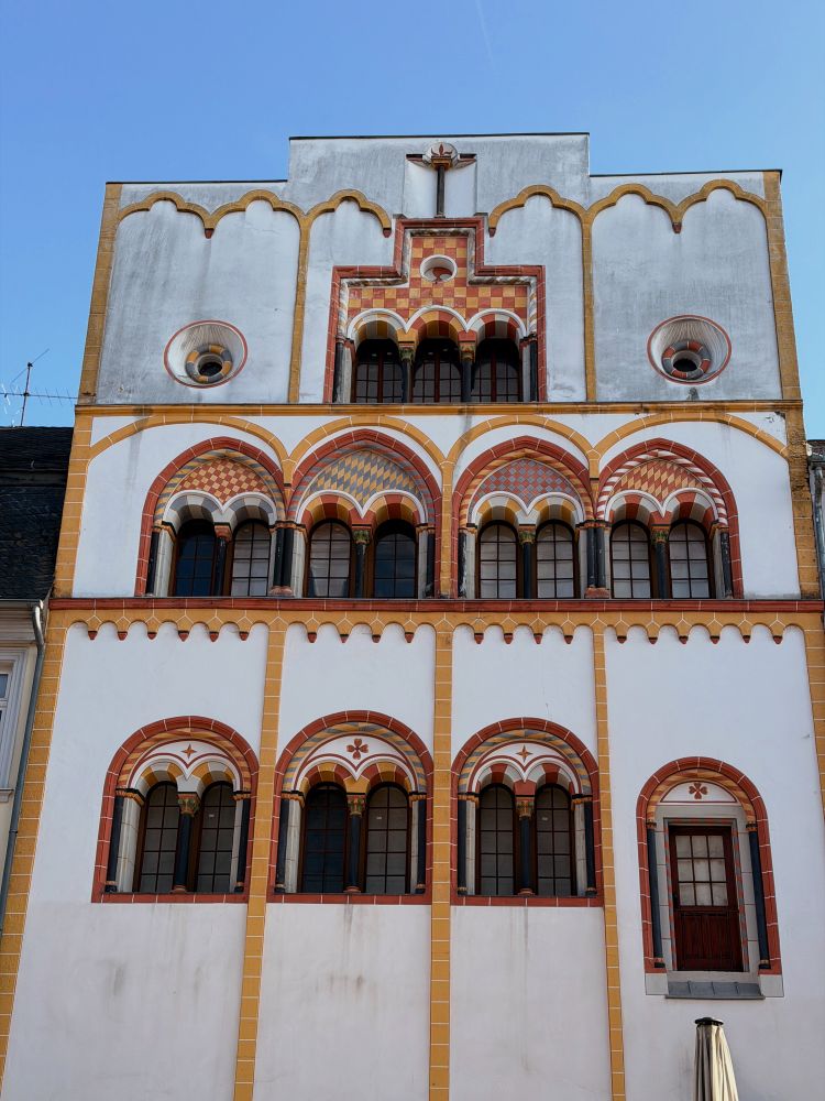 Weißer, Mittelalterlicher Wohnturm in Trier mit rundbogenfenstern verziert mit gelben und roten Steinen. Es ist das dreiköniginnenhaus 