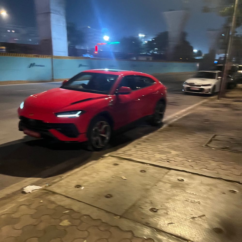 a red lamborghini urus parked on a curb looking extremely unremarkable. 