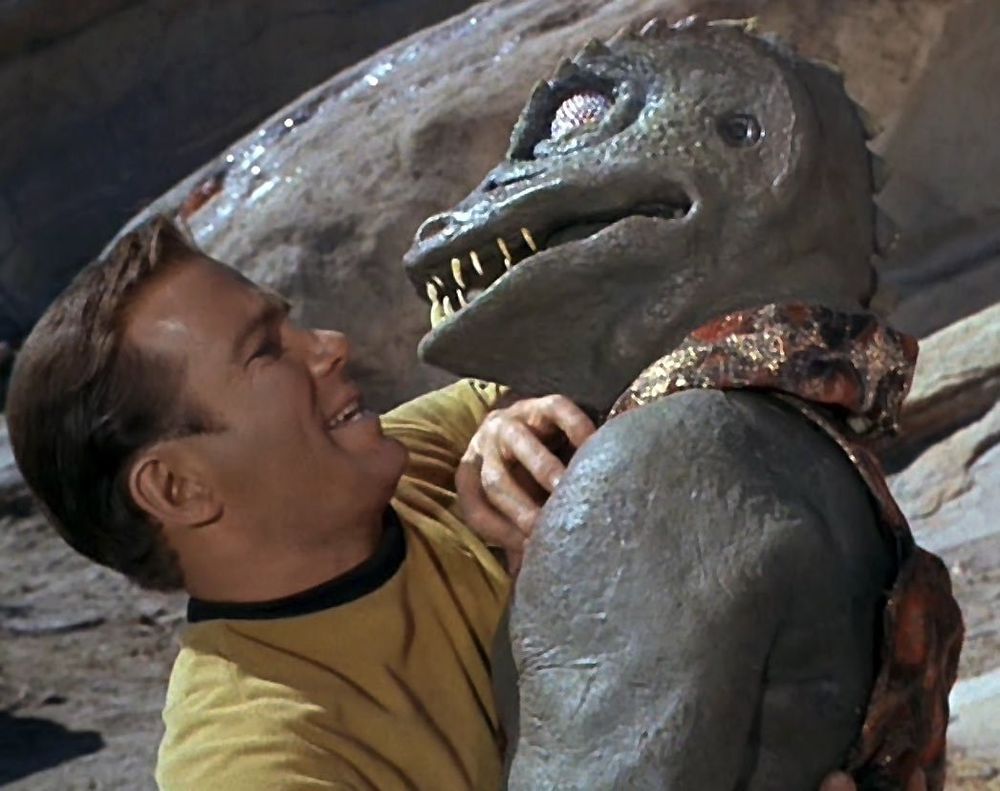Cpt. Kirk vs. The Gorn (humanoid lizard) from Star Trek: The Original series, in a clinch, their faces close to each other.