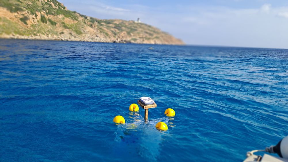 One drfiter floating on the sea, with yellow buoys. The sea is blue, there is a hill behind and the blue sky.