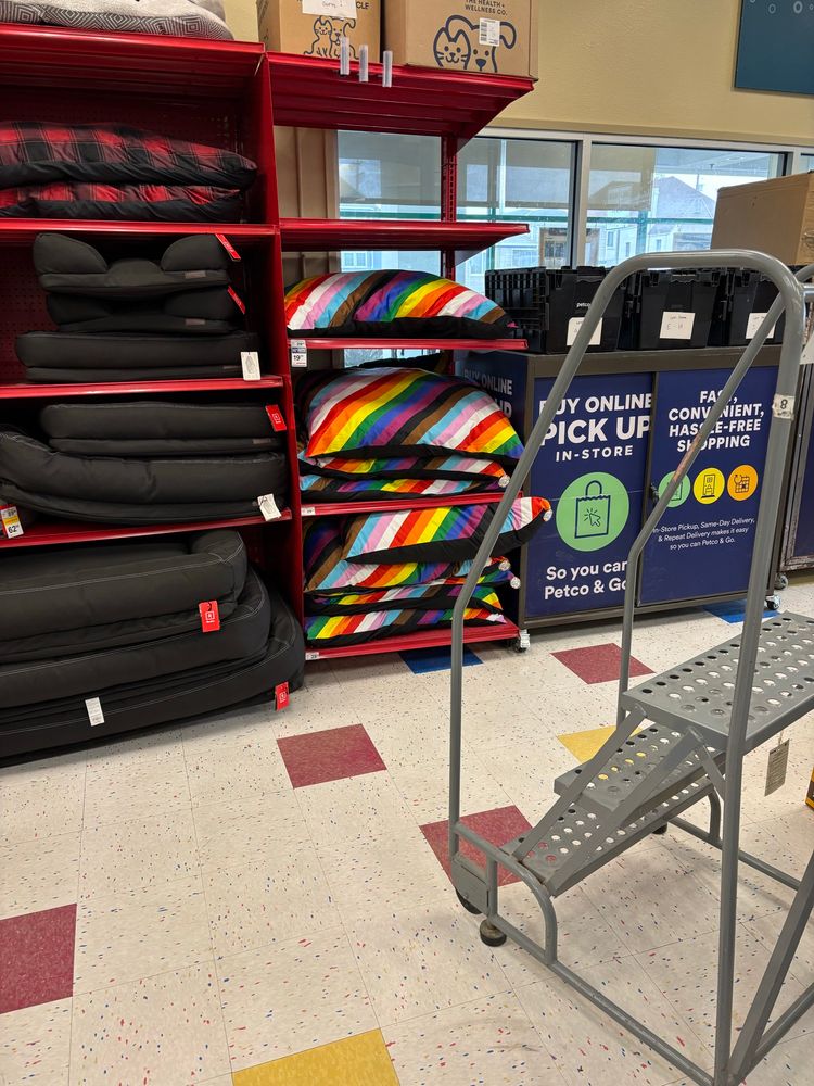 Red metal racks of dog beds in a Petco. The final rack has rainbow beds. 