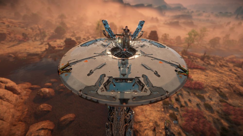 Aloy standing on the head of a Tallneck, about to override it. Behind you can see the area called Copper Deeps.