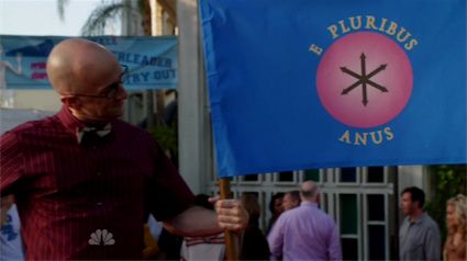An image from Community of Dean Pelton holding a blue flag with a pink circle around a black "asterisk" meant to look like an butthole, and surrounded by the words "E Pluribus Anus".