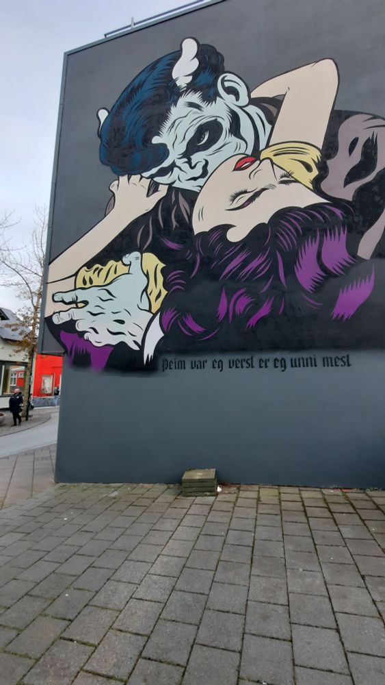 Street art mural of a comic book style man with horns seemingly sucking on the neck of a woman with closed eyes and cascading purple hair 