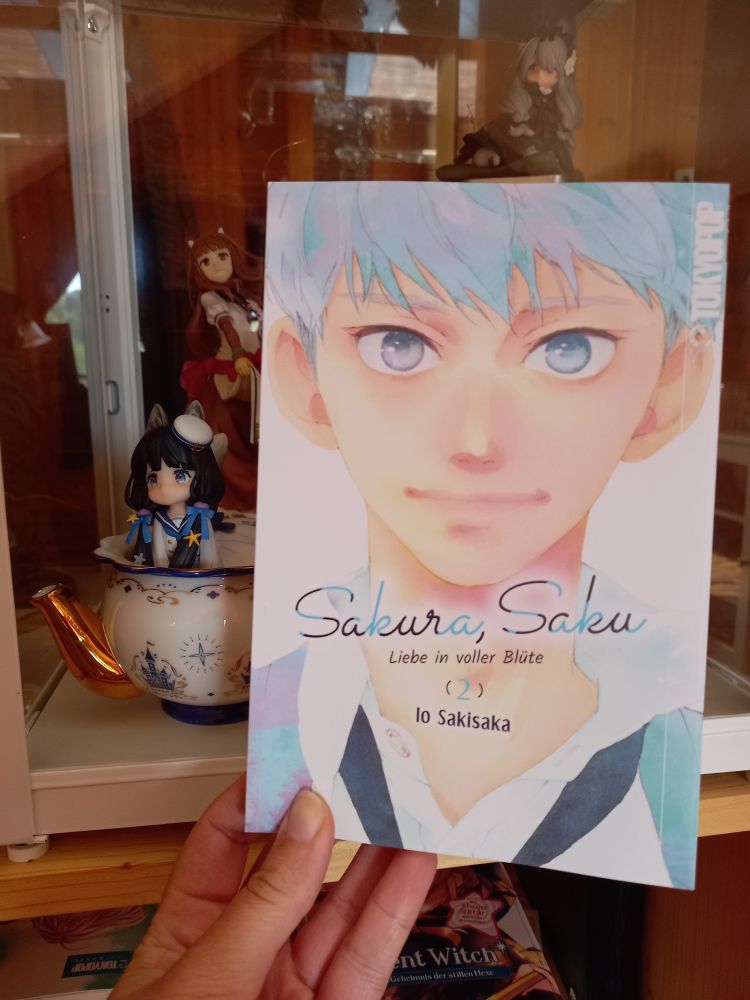 2nd volume of the manga callwd Sakura, Saku. The protagonist Sakura-kun smiles into the camera. His hair and his uniform is pastel blue.