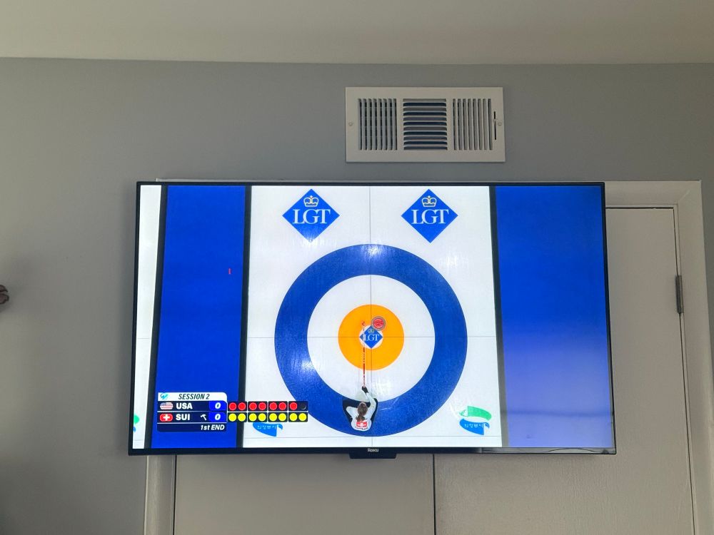 A photograph of the posters television showing curling tournament on it. The photo shows the end of the sheet of ice with one curling stone in the middle. The United States is playing Switzerland.