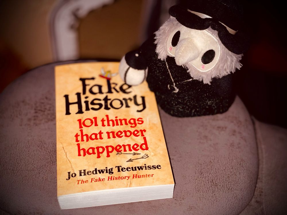 Image shows a book titled „Fake History“ by Jo Hedwig Teuwisse and a plush resembling a plague doctor.