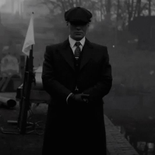 a man in a suit and hat stands in front of a river