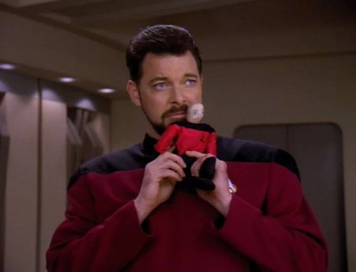 Riker holding a tiny doll replica of Picard on Captain Picard Day