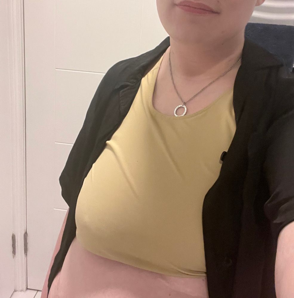 Leo is taking a selfie. His black button up is unbuttoned, revealing his binder. He is wearing a silver necklace with a ring charm. His chin and some of his lips are visible, he’s smiling.